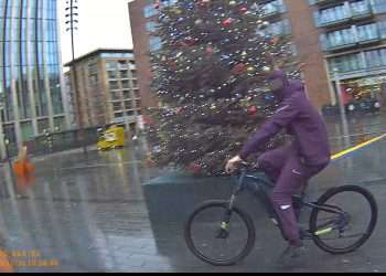 A balaclava-wearing youth cycling through Canada Water