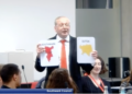 Cllr Livingstone holding up cards of Lib Dem controlled boroughs and asking councillors if council tax is higher or lower